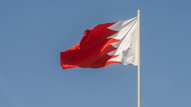 The Bahrain national flag capturing the vibrant red and white design against a clear blue sky.