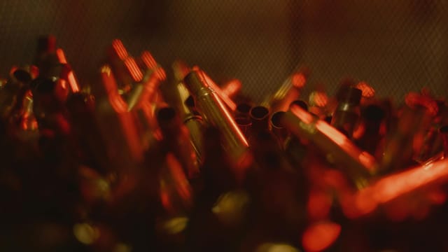 A close-up view of bullet casings illuminated by a warm red light, creating a dramatic abstract scene.