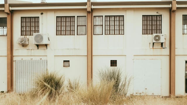 Facade of an urban industrial building with large windows and air conditioning units.
