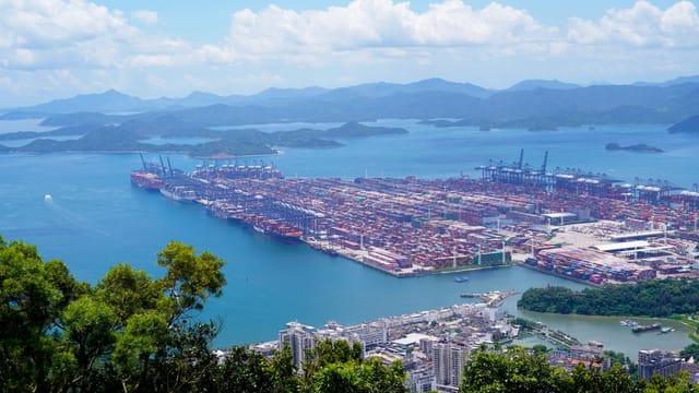 Aerial image of a bustling industrial port with containers in a scenic coastal setting.