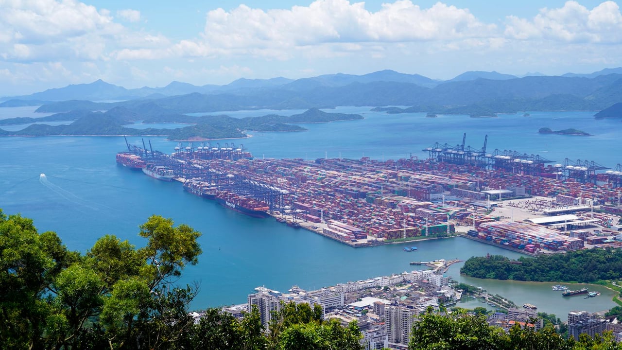 Aerial image of a bustling industrial port with containers in a scenic coastal setting.