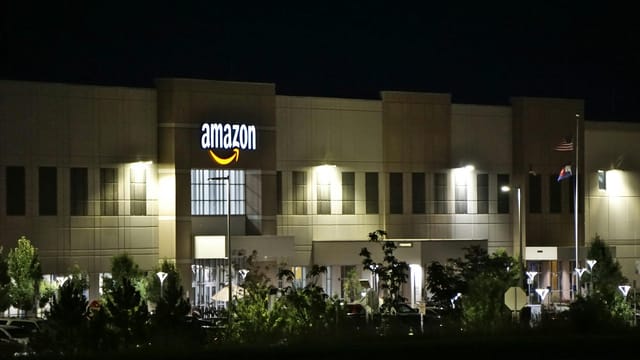 Amazon warehouse building illuminated at night with trees and signage.