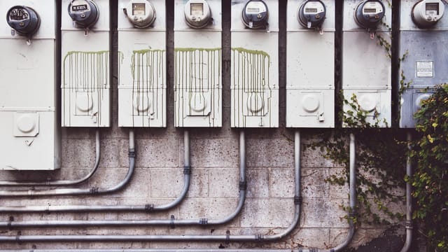 Array of outdoor electric meters on a brick wall with vines.