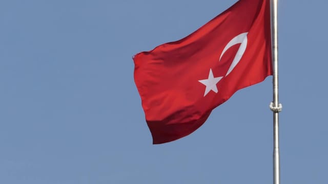 Turkish national flag waving against a clear blue sky, symbolizing national pride.