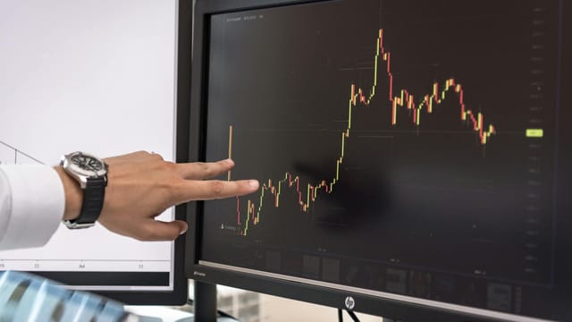 Detailed view of a hand pointing at a cryptocurrency trading graph on a monitor.