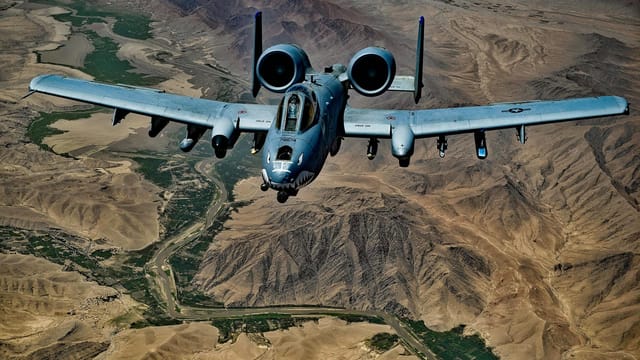 A military aircraft flying over a vast desert landscape with dramatic views.