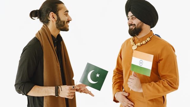 Two men, holding Indian and Pakistani flags, engage in friendly conversation.