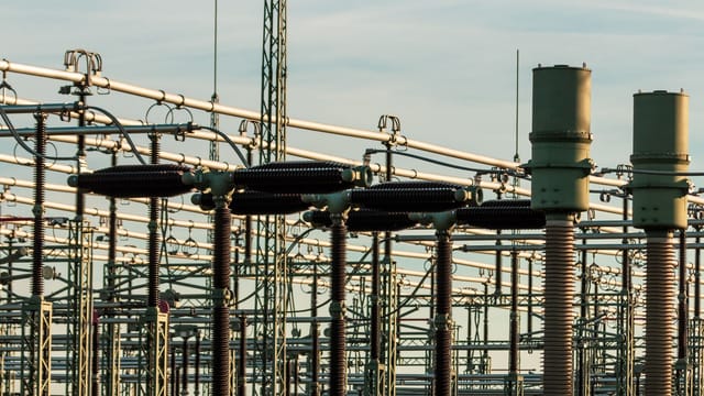 Detailed view of electrical substation with high voltage equipment and insulators against a clear sky.