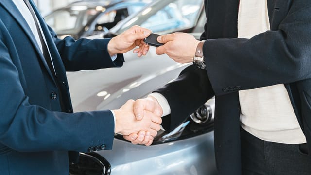 Two businessmen shaking hands and exchanging car keys in a dealership. Symbolizes a successful deal.