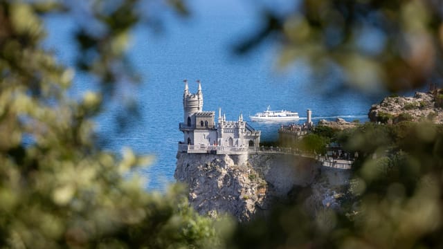 Swallow's Nest Castle perched on a cliff with the Black Sea backdrop, surrounded by lush greenery.