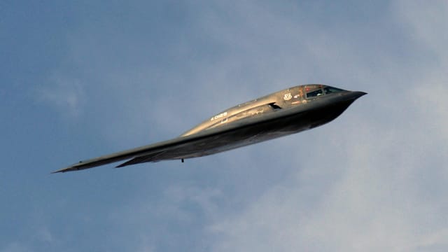 A stealth bomber aircraft soaring smoothly through a clear blue sky during the day.