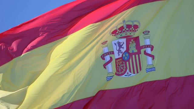 Vibrant Spanish flag waving against a clear blue sky in Cádiz, Andalucía.
