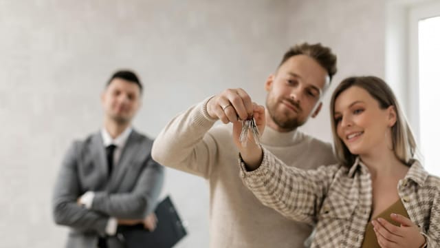 A joyful couple holding keys to their new home with a realtor in the background.