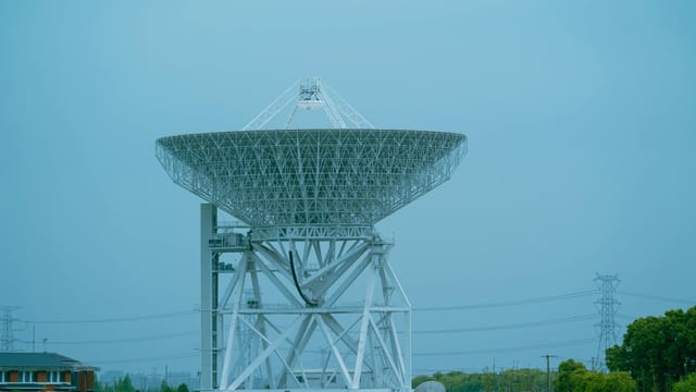 A large white satellite dish standing outdoors in a rural area, used for communication.