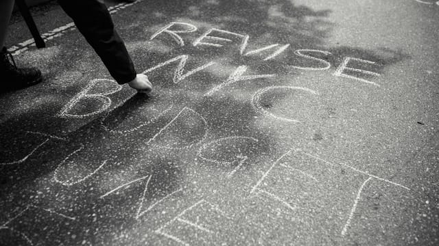 Person writing protest message with chalk on streets of NYC, urging budget revision.