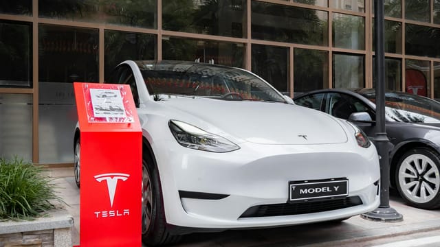 Tesla Model Y parked outdoors with a red display stand in front. Modern and sleek automotive design.