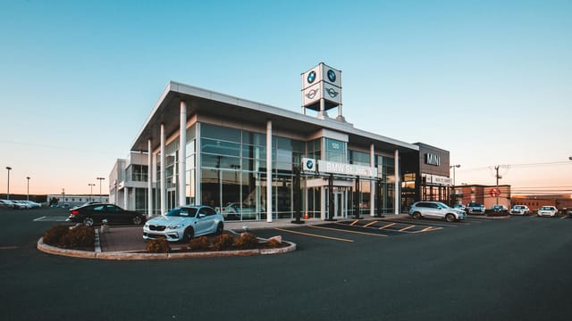 A modern BMW car dealership in a city with luxury cars and clear blue sky.