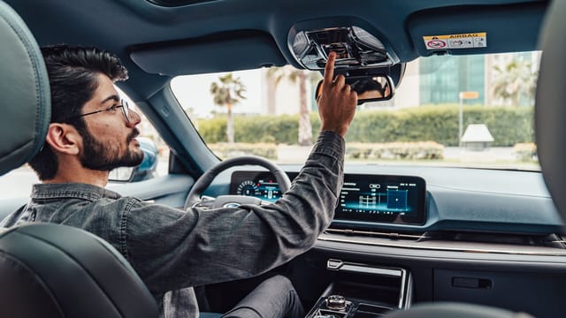 A man adjusts the interior features of a modern car while driving in Erbil, Iraq.