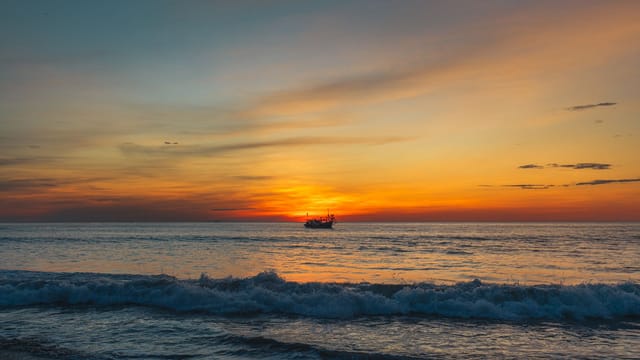 Peaceful ocean sunset with a boat silhouetted on the horizon in Quảng Trị, Vietnam.