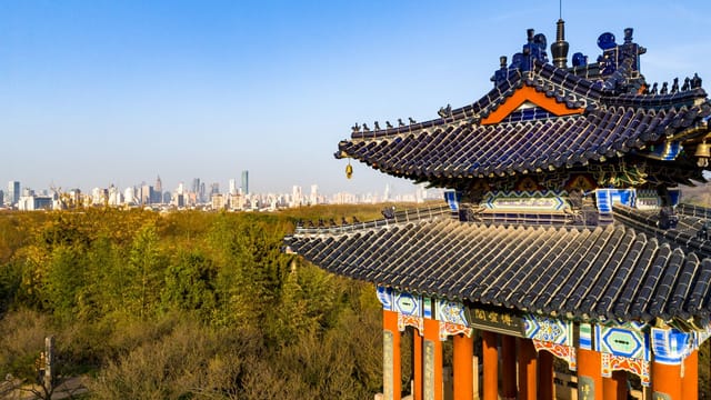 Scenic view of a traditional Chinese pavilion with the Nanjing city skyline in the background.