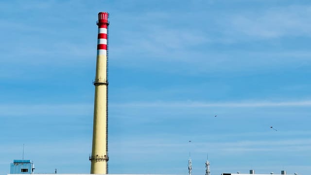 Tall industrial chimney with red and white stripes against a clear blue sky.