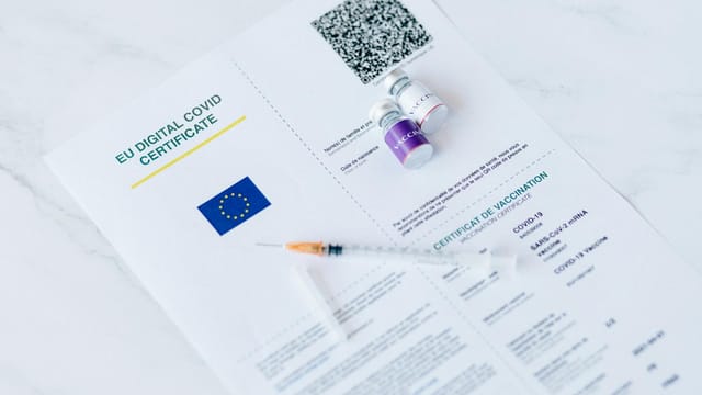 EU digital COVID certificate with vaccine vials and syringe on a white background.
