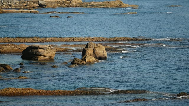 Scenic view of rocky shoreline in Keelung, Taiwan with calm ocean waters under daylight.