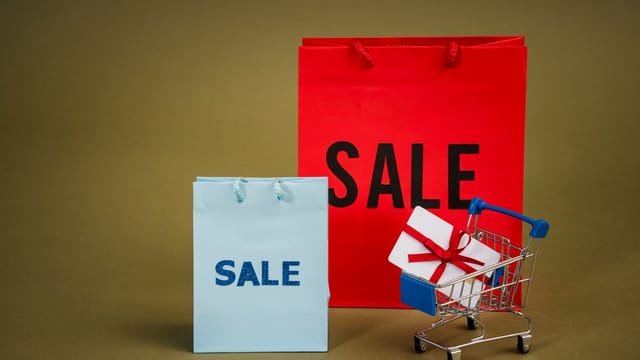 Bright sale bags with a gift in a shopping cart against a neutral background.