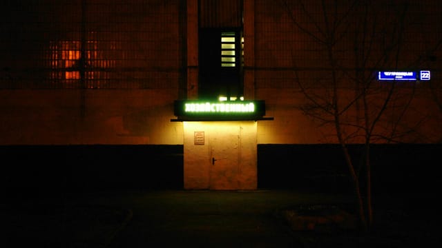 A dark urban scene illuminated by a neon sign, creating a moody atmosphere.