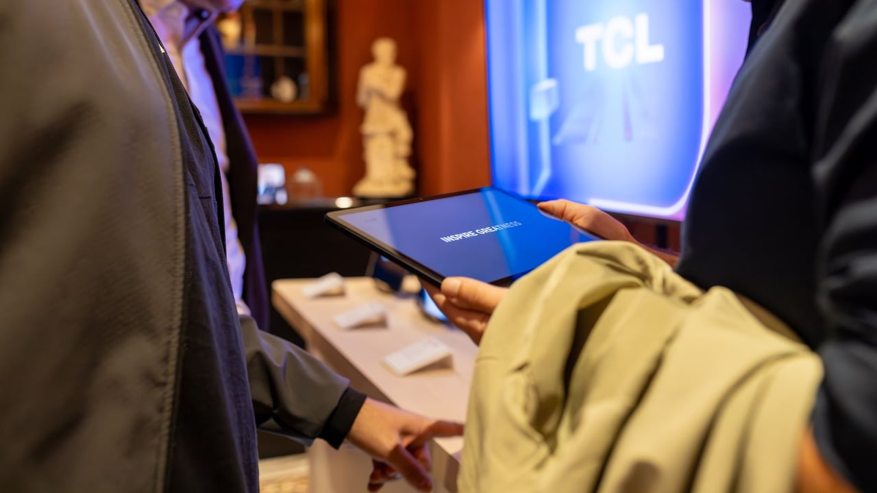 Close-up of individuals exploring a tablet device at a tech exhibit by TCL, highlighting interaction and modern technology.