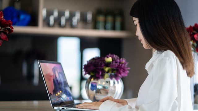 Asian woman working on her laptop in a stylish workspace with floral decor.