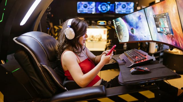 Young woman enjoying computer gaming at home with a high-tech gaming setup and smartphone.