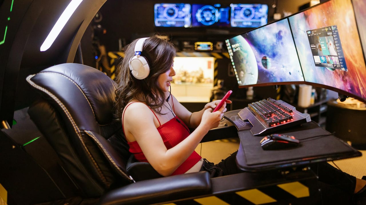 Young woman enjoying computer gaming at home with a high-tech gaming setup and smartphone.