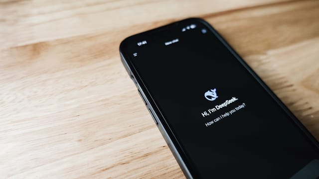Close-up of a smartphone with DeepSeek virtual assistant on screen, placed on a wooden surface.
