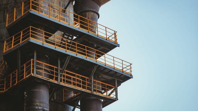 Close-up view of industrial metal balconies and pipes against a clear sky.