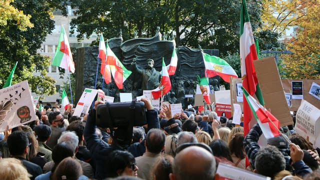 Protest gathering in central Stockholm featuring Iranian flags and banners.
