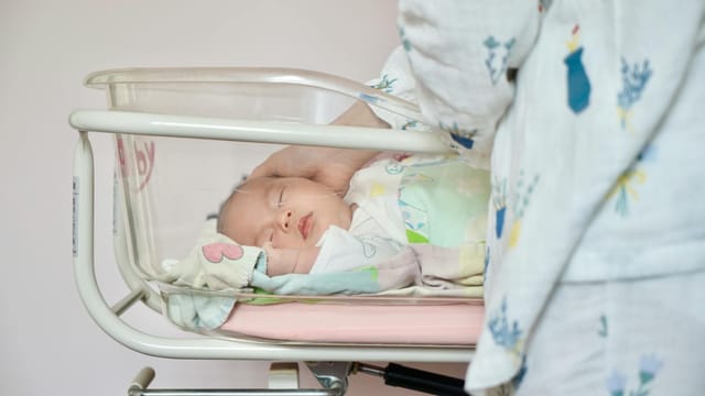 A tender moment of a newborn baby sleeping peacefully in a hospital bassinet being gently touched by a parent.