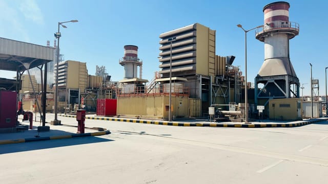 A modern power plant with turbines and chimneys under a clear blue sky in Saudi Arabia.