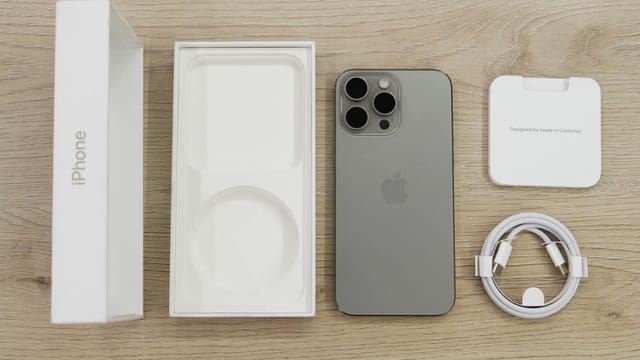 Flat lay view of the newest Apple iPhone model, box, and charging accessories on a wooden table.