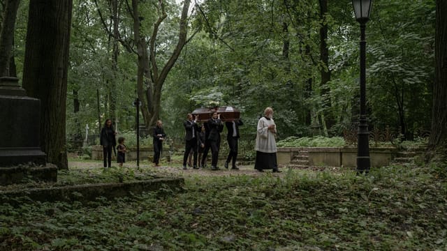 A funeral procession with mourners carrying a coffin through a serene forest cemetery.