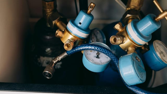 Detailed view of blue and brass gas pressure regulators with gauges and tubing in an industrial setting.