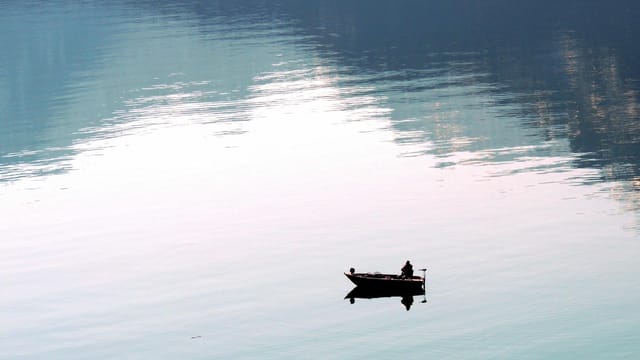 A lone fisherman in a small boat on the peaceful waters of Lake Wolfgang, Austria.