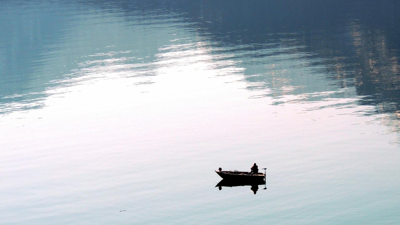 A lone fisherman in a small boat on the peaceful waters of Lake Wolfgang, Austria.