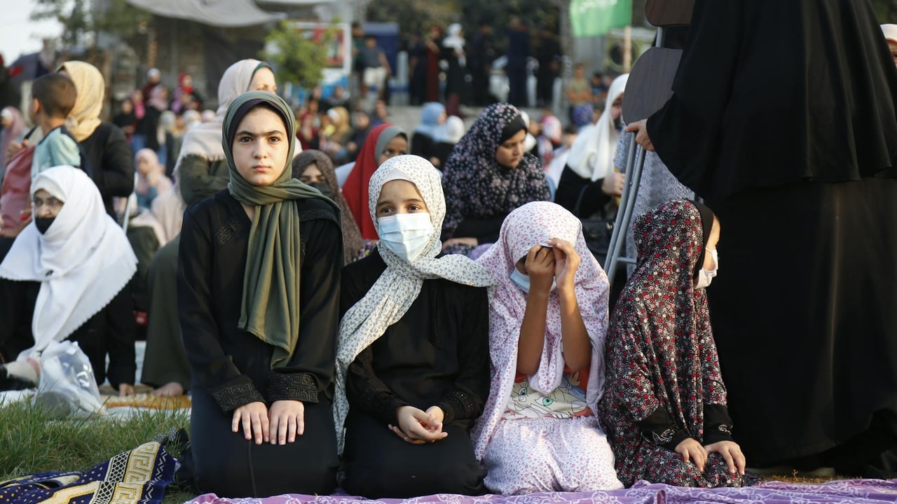 Muslim women in hijabs gather outdoors for prayer in Gaza, highlighting cultural and religious traditions.