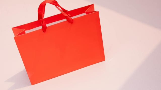 Vibrant orange paper shopping bag on a light pastel surface. Perfect for retail and branding visuals.