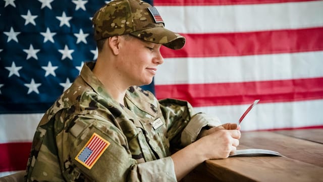 Soldier in uniform with US flag background, reflecting on memories.