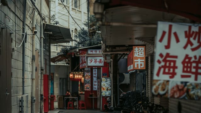 A vibrant urban alleyway lined with street vendors and signage in an Asian city.