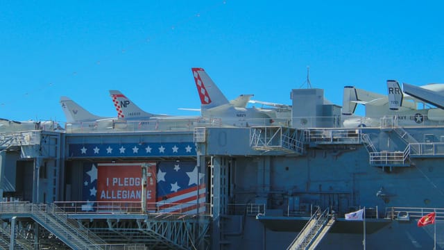 A view of a military aircraft carrier deck with fighter jets and patriotic banner.