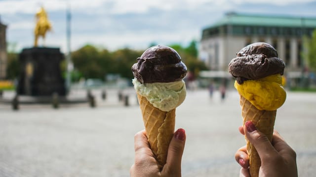 Colorful ice cream cones held up in a vibrant Dresden square, showcasing delightful flavors.