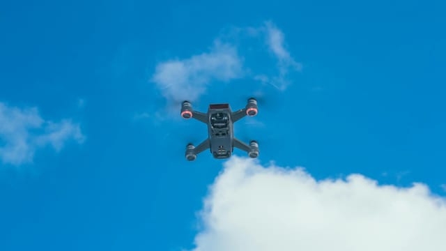 A modern quadcopter drone navigating through a bright blue sky with clouds. Ideal for tech and innovation themes.